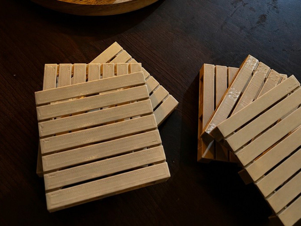 3D printed miniature pallet coasters in cream PETG on a dark wooden table